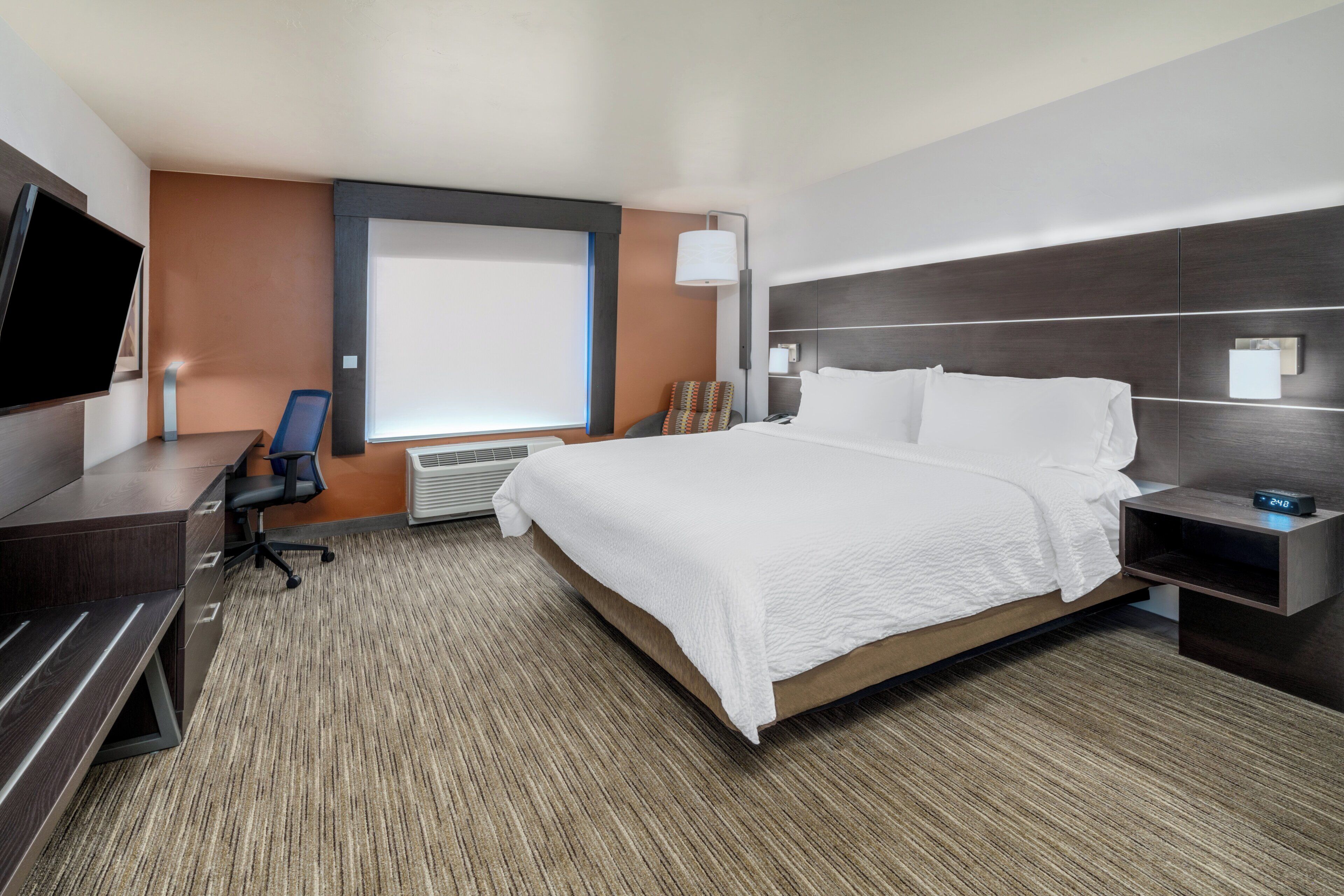 Ein Hotelzimmer mit einem großen Bett, einem Schreibtisch mit Stuhl, einem Flachbildfernseher und einem Fenster mit Jalousien.