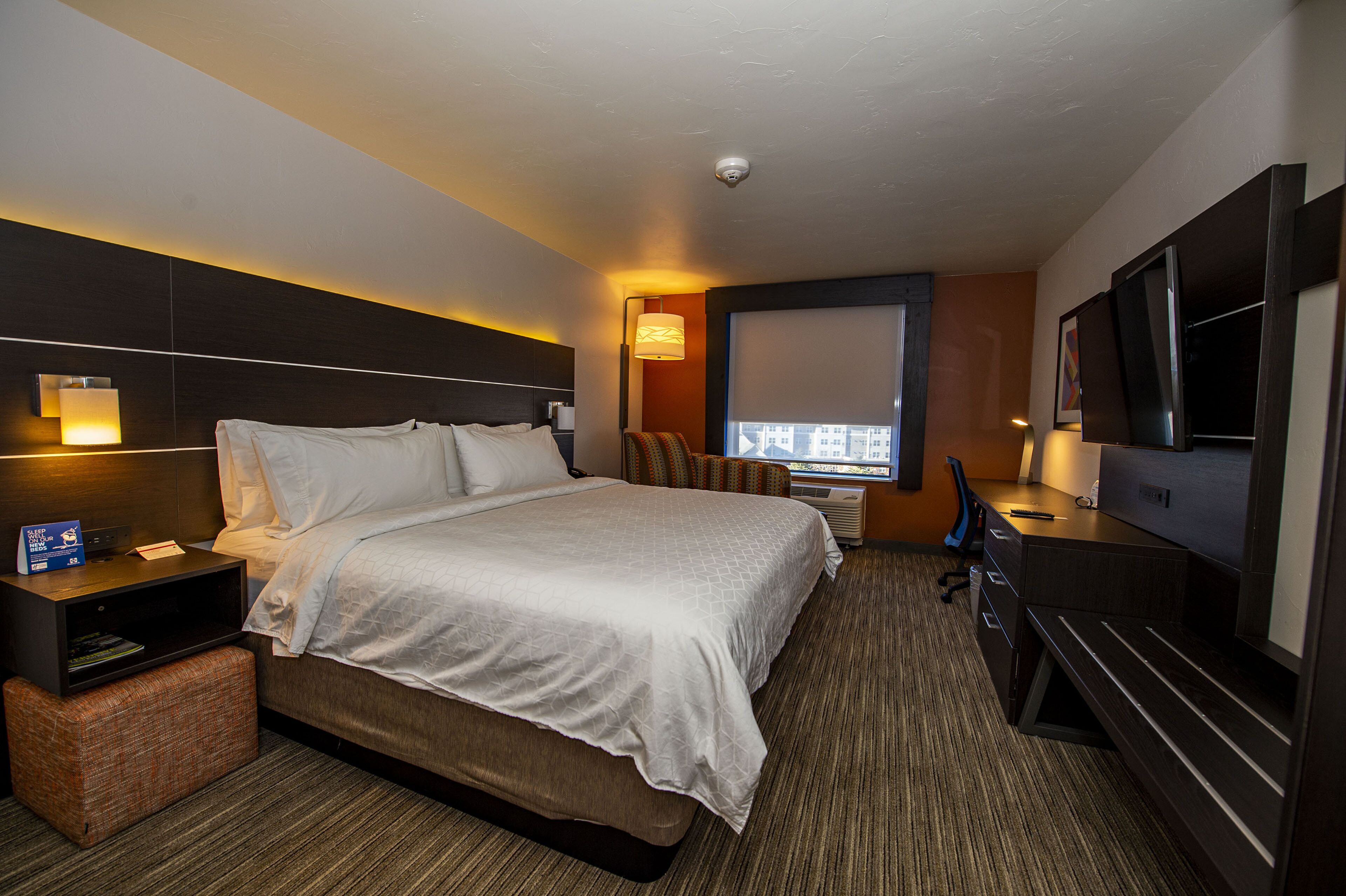 A hotel room with a large bed, a desk, a television, and a window with a city view.