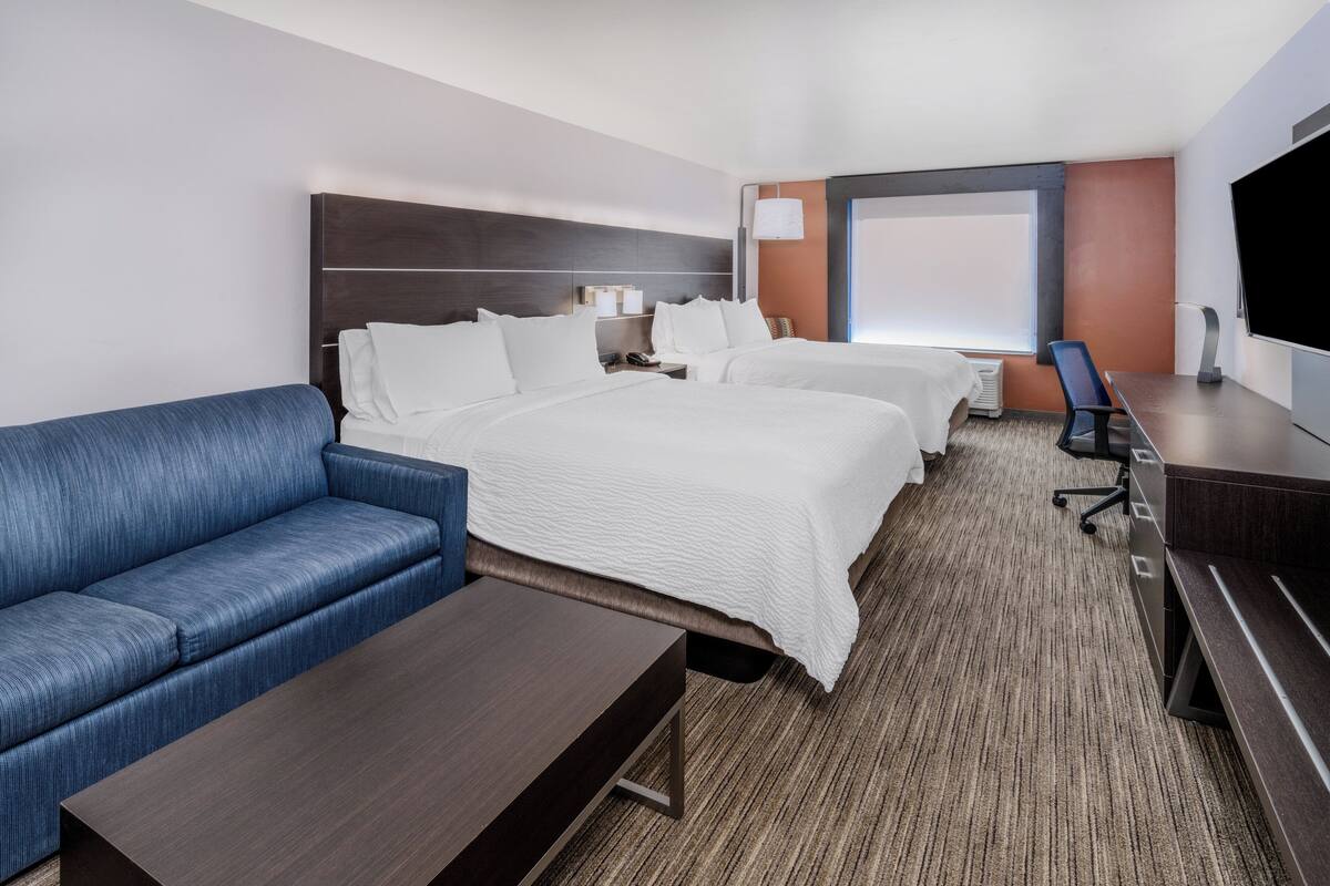 A hotel room with a large bed, a sofa, a desk, and a TV.