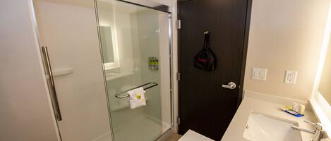 A modern bathroom with a glass-enclosed shower, a dark wooden door, and a white sink with toiletries.