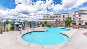 Piscina com design curvo, cercada por grade, adjacente a um edifício com várias janelas e varandas.