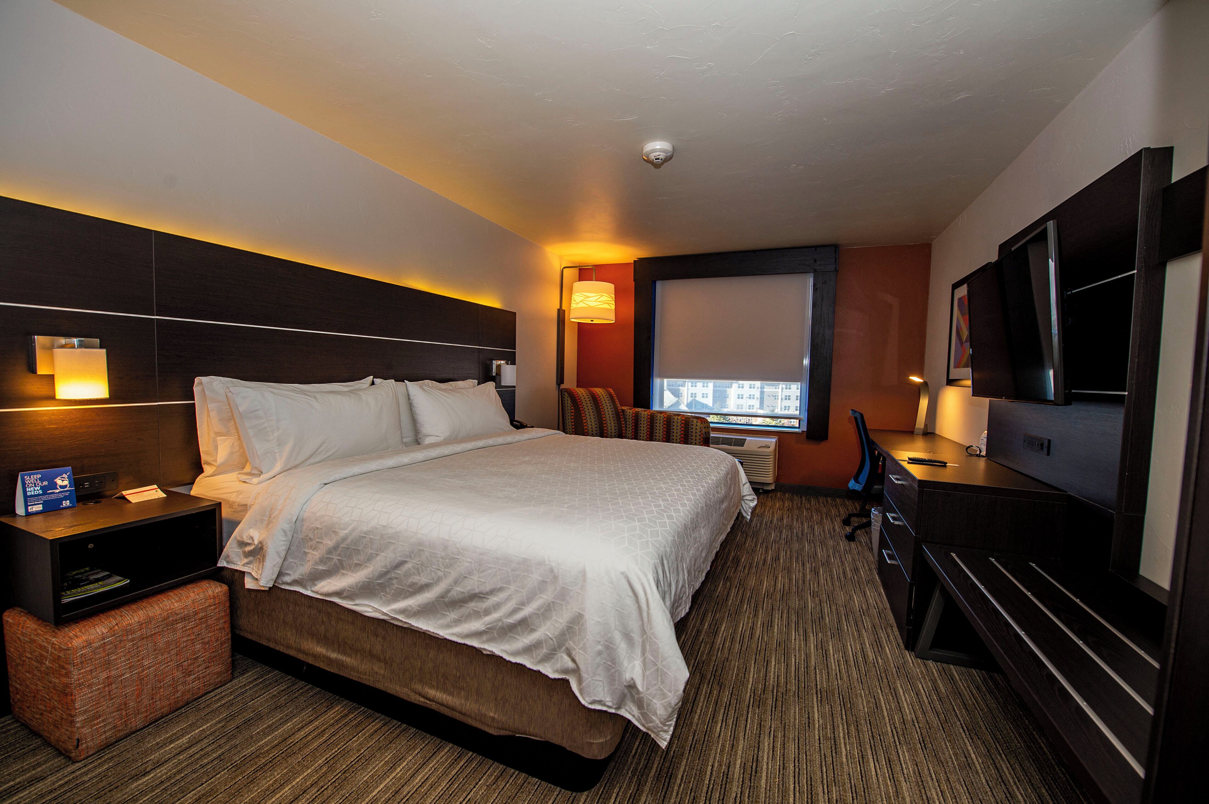 A hotel room with a bed, bedside table, lamp, TV, and a window with a view.