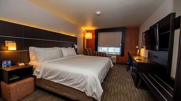 A hotel room with a bed, bedside table, lamp, TV, and a window with a view.