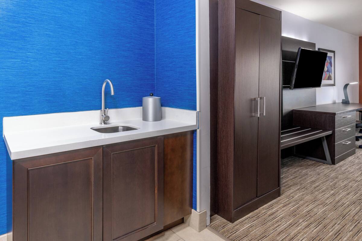 A modern bathroom with a blue textured wall, a sink with a faucet, a toilet, and a cabinet with drawers.