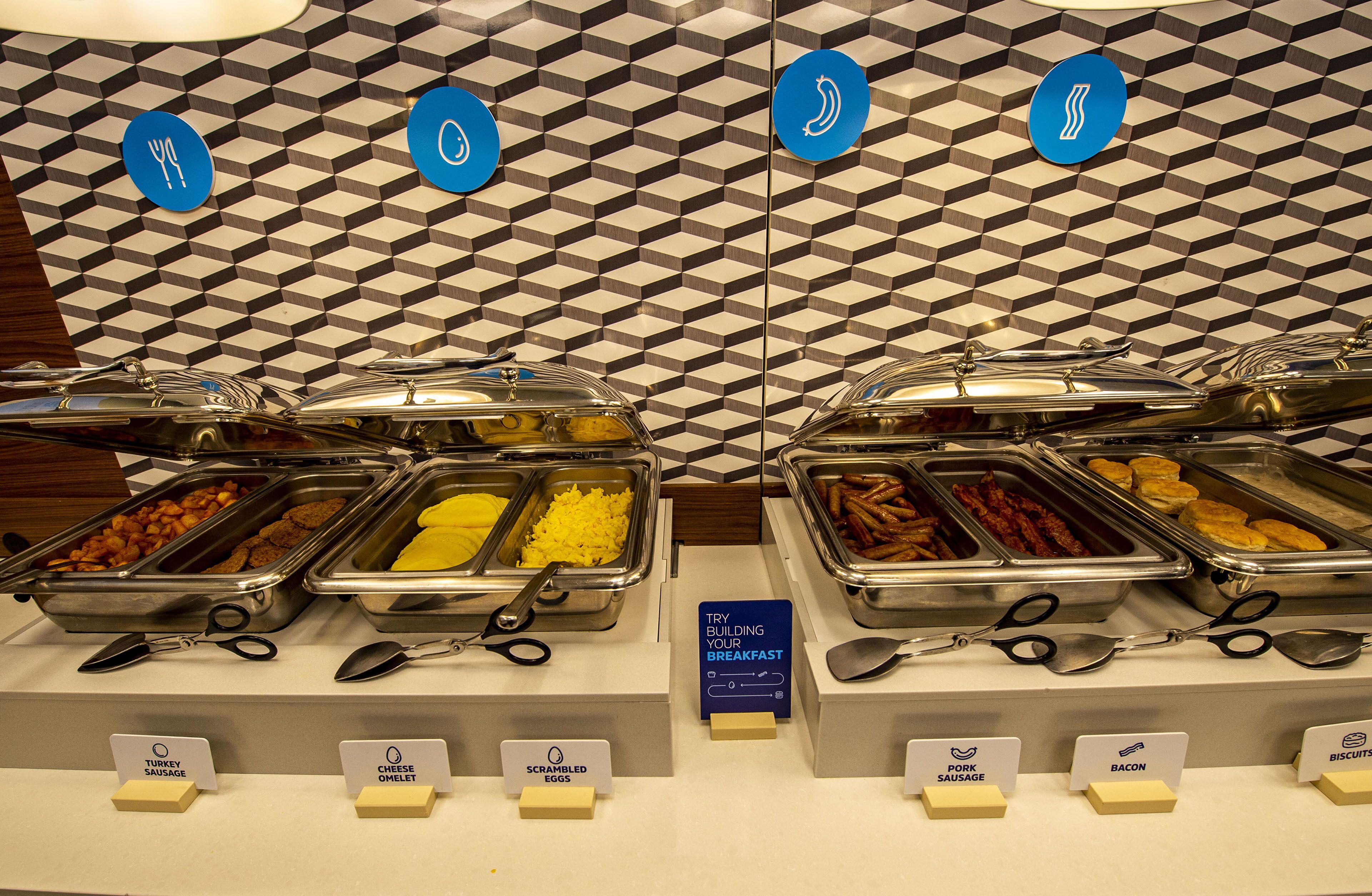 A buffet with various food options including scrambled eggs, turkey sausage, cheese omelet, bacon, and biscuits.