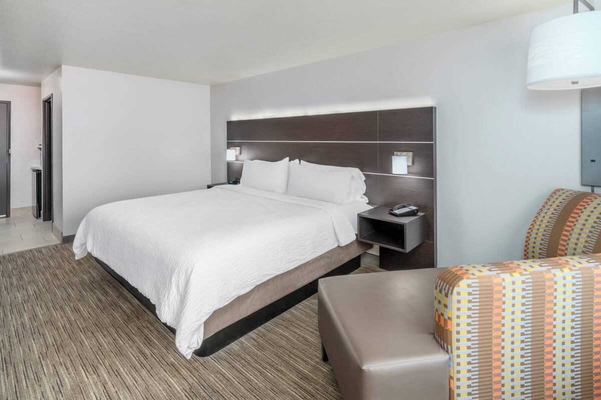 A modern hotel room with a large bed, a nightstand, a chair, and a lamp.