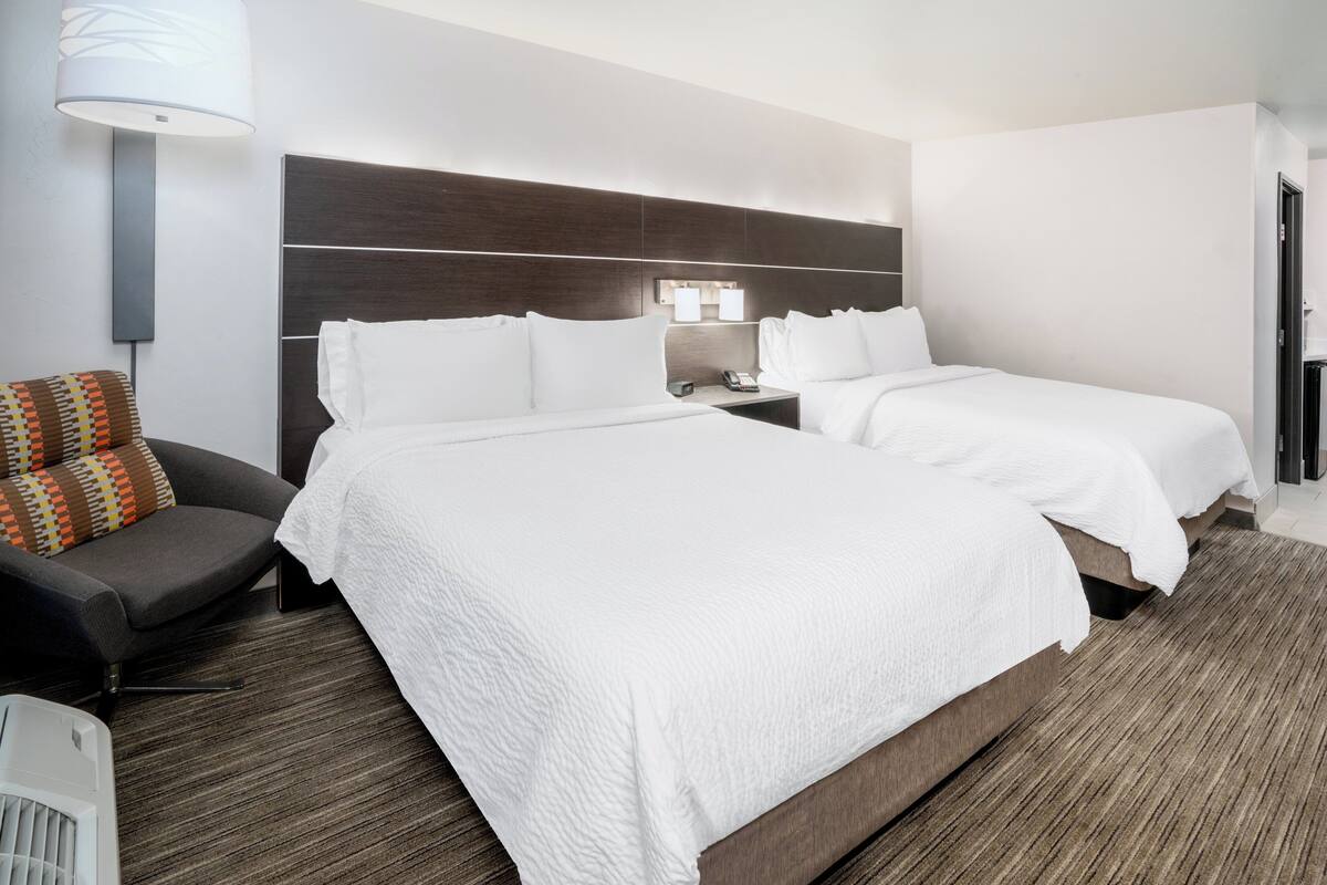 A hotel room with two beds, a desk, a chair, and a lamp.