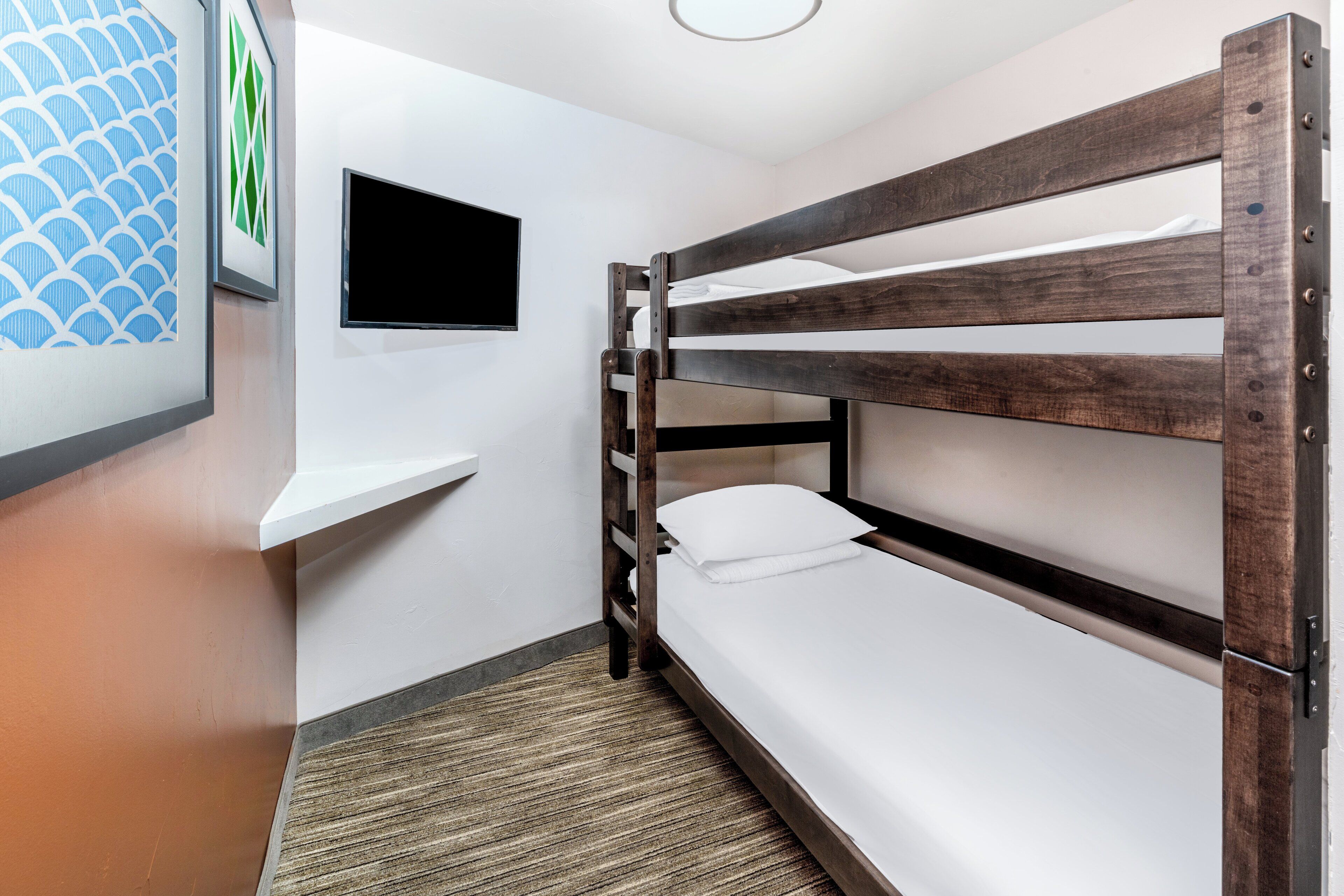 Une chambre avec des lits superposés, un téléviseur à écran plat fixé au mur, une petite étagère et un tapis à motifs.