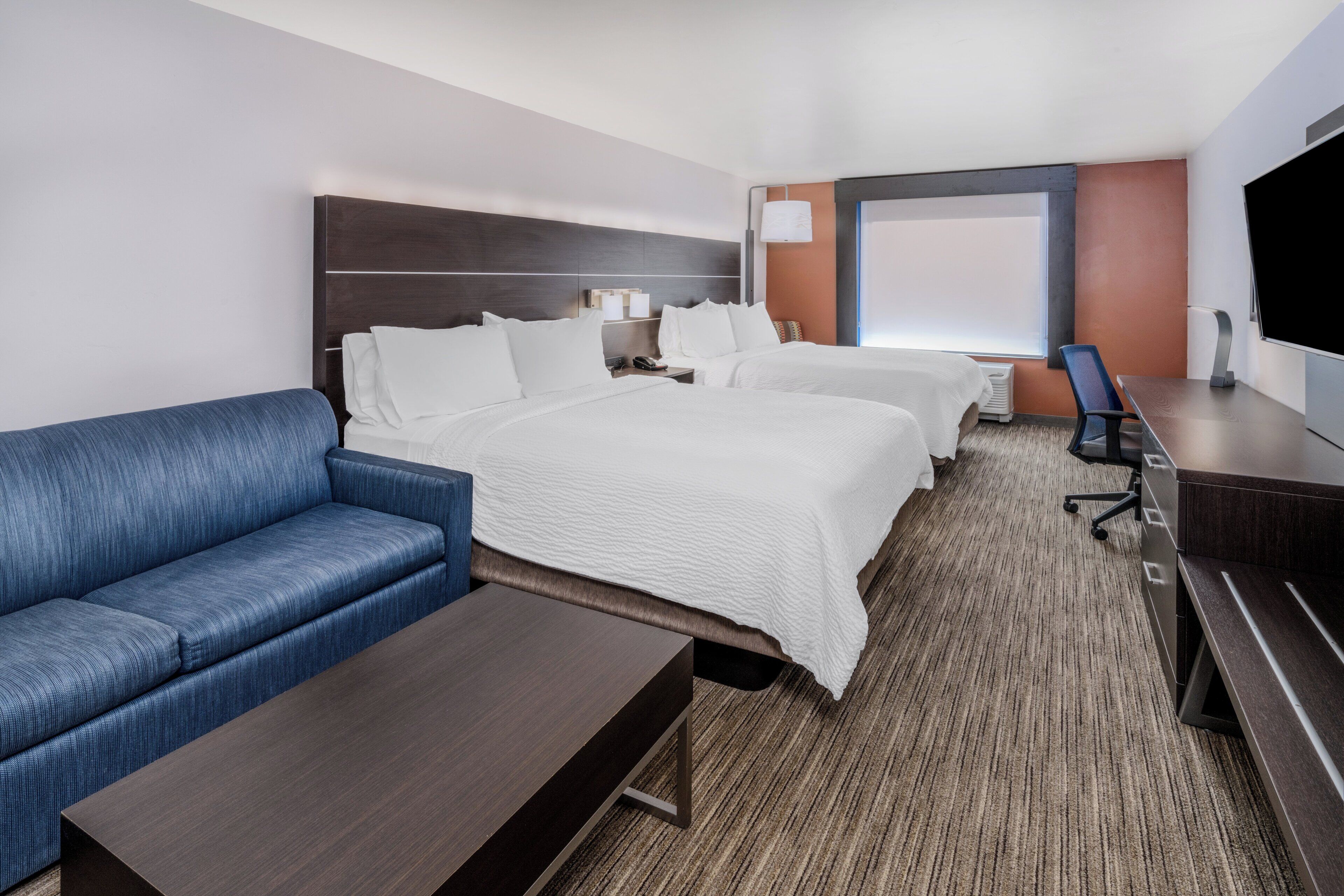 A hotel room with a large bed, a sofa, a desk, and a TV.