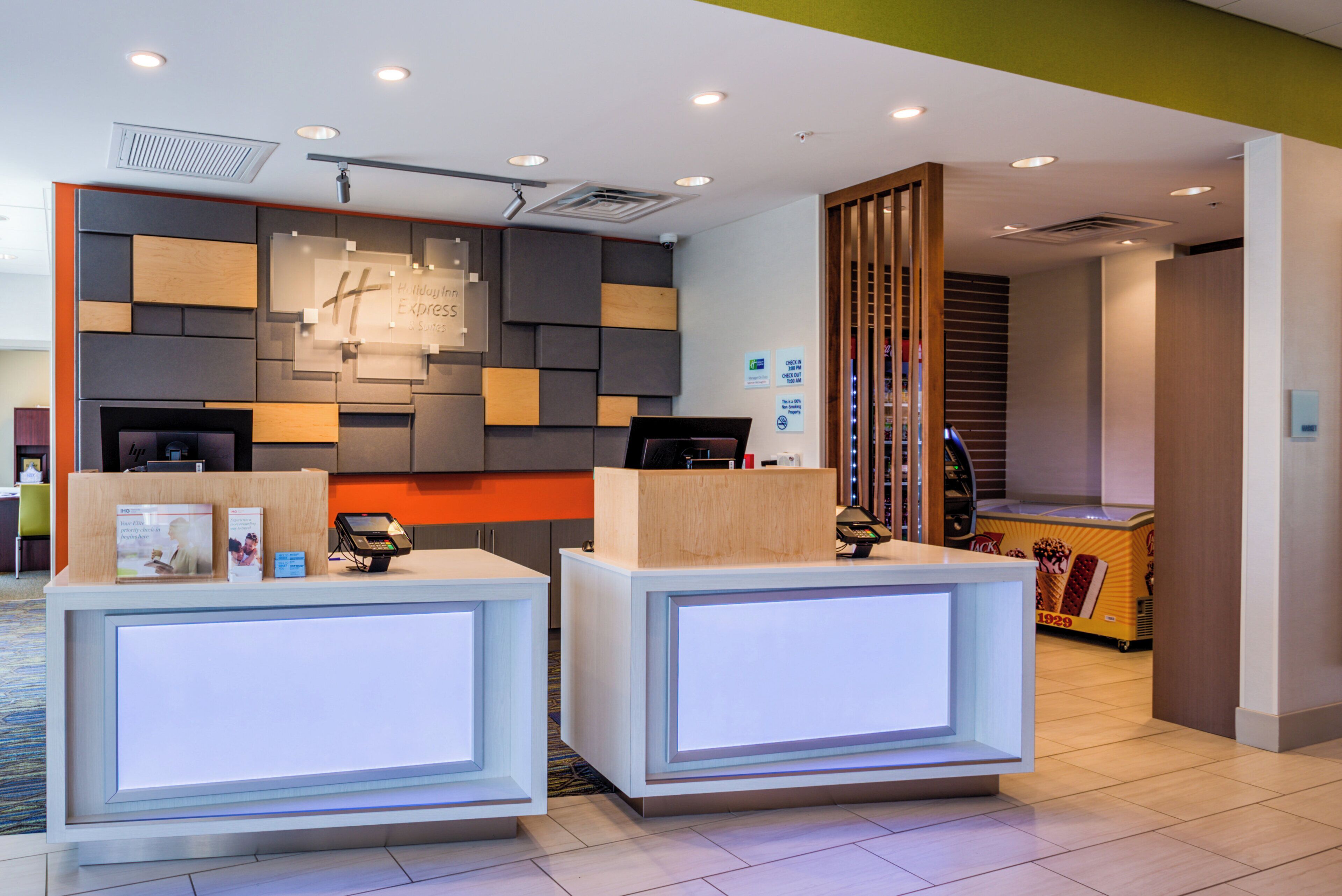 Área de recepção com design moderno, incluindo balcão de check-in, display digital e placa com o nome do hotel.