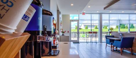 Het interieur van een koffiebar, met espresso machines, een balie en een uitzicht op het buitengebeuren door grote ramen.
