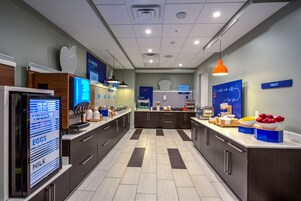 A modern kitchen with a digital menu display, a fruit section, and a counter with various food items.