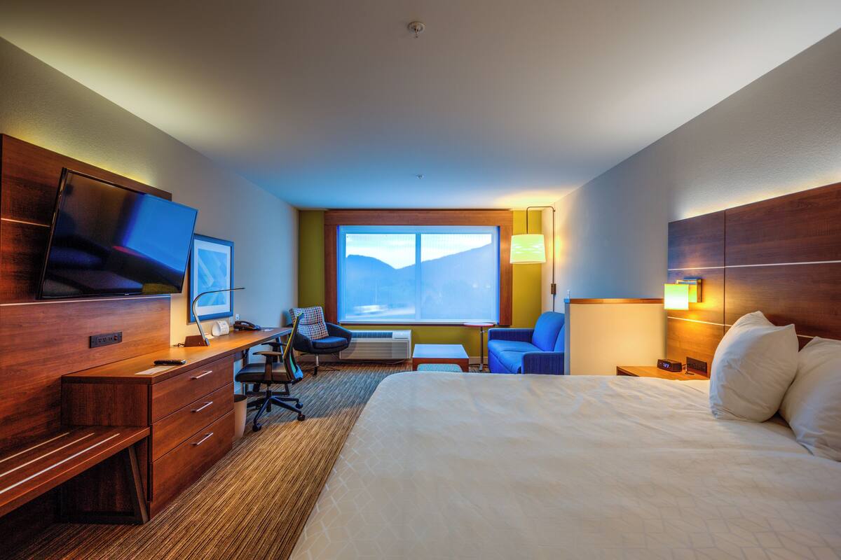 A hotel room with a bed, desk, chair, TV, and a large window.