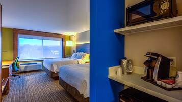 A hotel room with two beds, a desk with a computer, a coffee machine, and a view of the outdoors.