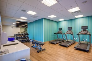 Et fitnesscenter med løbebånd, bænk og styrketræningsudstyr.