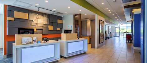 A hotel reception area with a modern design, including a reception desk, a digital check-in kiosk, and a wall-mounted sign.