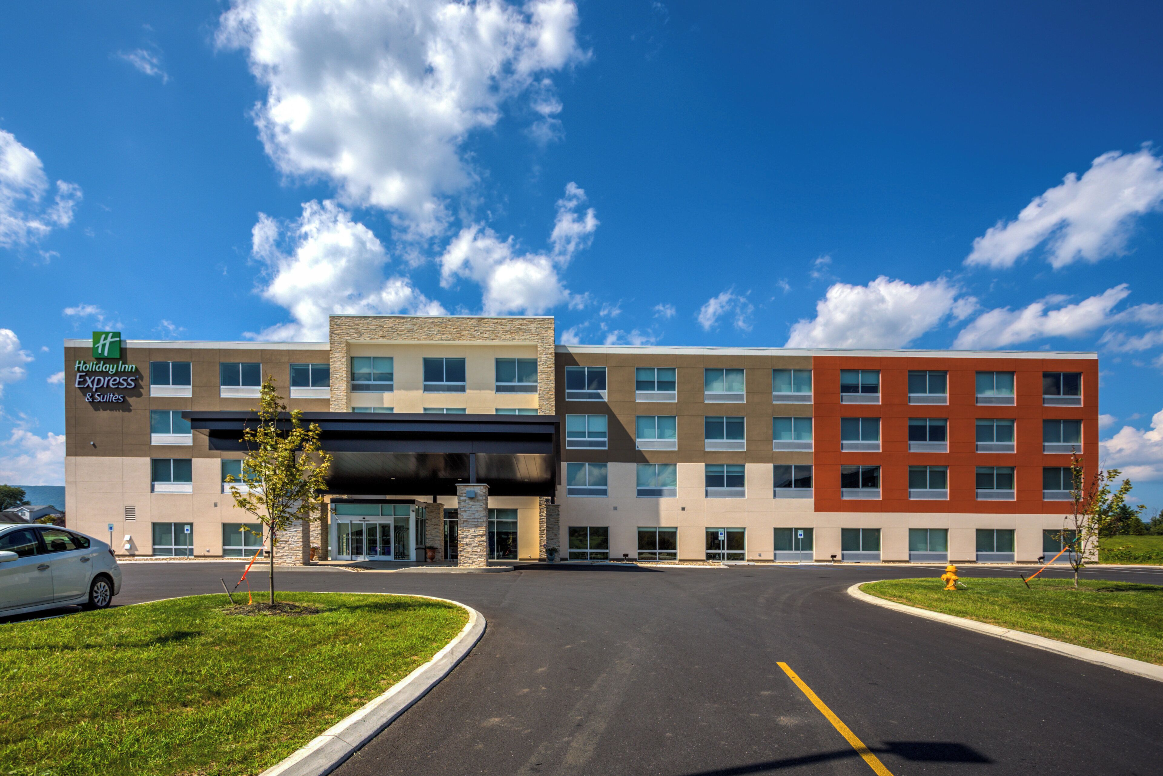 Un hotel Holiday Inn Express & Suites con diseño moderno, con fachadas de ladrillo y vidrio, una entrada cubierta y un estacionamiento con hidrante.