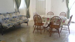 A living room with a sofa, a dining table with chairs, and a door. - Casa en PlayaDelCarmen 510 by Sinbad (Playa del Carmen)