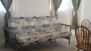 A room with a sofa and a wooden chair, a window with curtains, and a tiled floor. - Casa en PlayaDelCarmen 510 by Sinbad (Playa del Carmen)