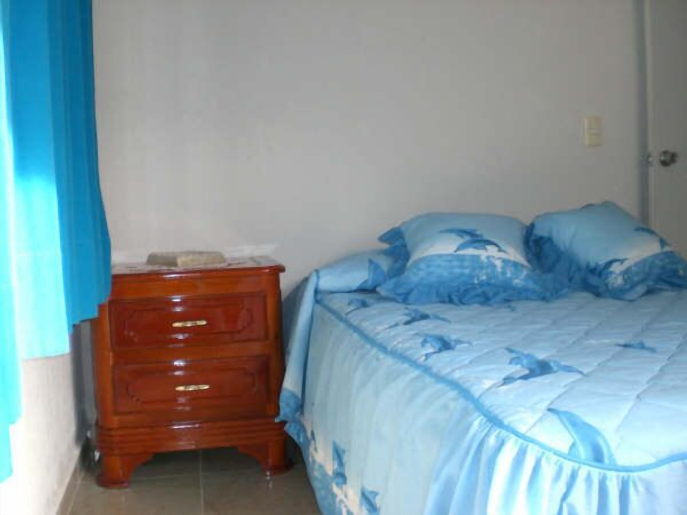 A bedroom with a bed, a wooden nightstand, and a blue curtain.