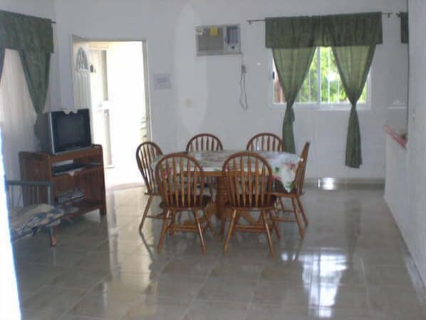 A dining area with a tiled floor, wooden chairs, a table, and a television on a wooden stand.