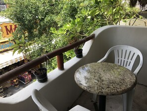 Een balkon met een witte stoel en een klein tafeltje, omringd door potplanten en een houten balustrade.