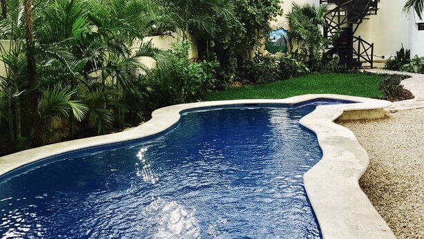 A swimming pool surrounded by lush greenery and a multi-story building with a spiral staircase. - Condo Centro Playa del Carmen 509 (Playa del Carmen)