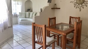 A dining area with a glass-top table and wooden chairs, a ceiling fan, a sun decoration, and a sofa in the background. - Condo Centro Playa del Carmen 509 (Playa del Carmen)