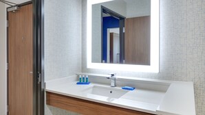 Une salle de bain moderne avec un grand miroir, un lavabo blanc et un meuble-lavabo en bois.
