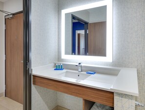 Un baño moderno con un espejo grande, lavamanos blanco y tocador de madera.