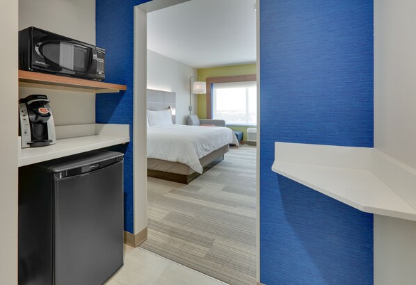Habitación de hotel con cama, microondas, cafetera y refrigerador pequeño.