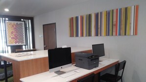 Un comptoir d’accueil équipé d’une imprimante, d’un ordinateur et d’une tablette. On y trouve une porte et une œuvre d’art colorée accrochée au mur.