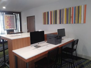 Un mostrador de recepción con una impresora, una computadora y una tableta. Se ve una puerta y una obra de arte colorida en la pared.