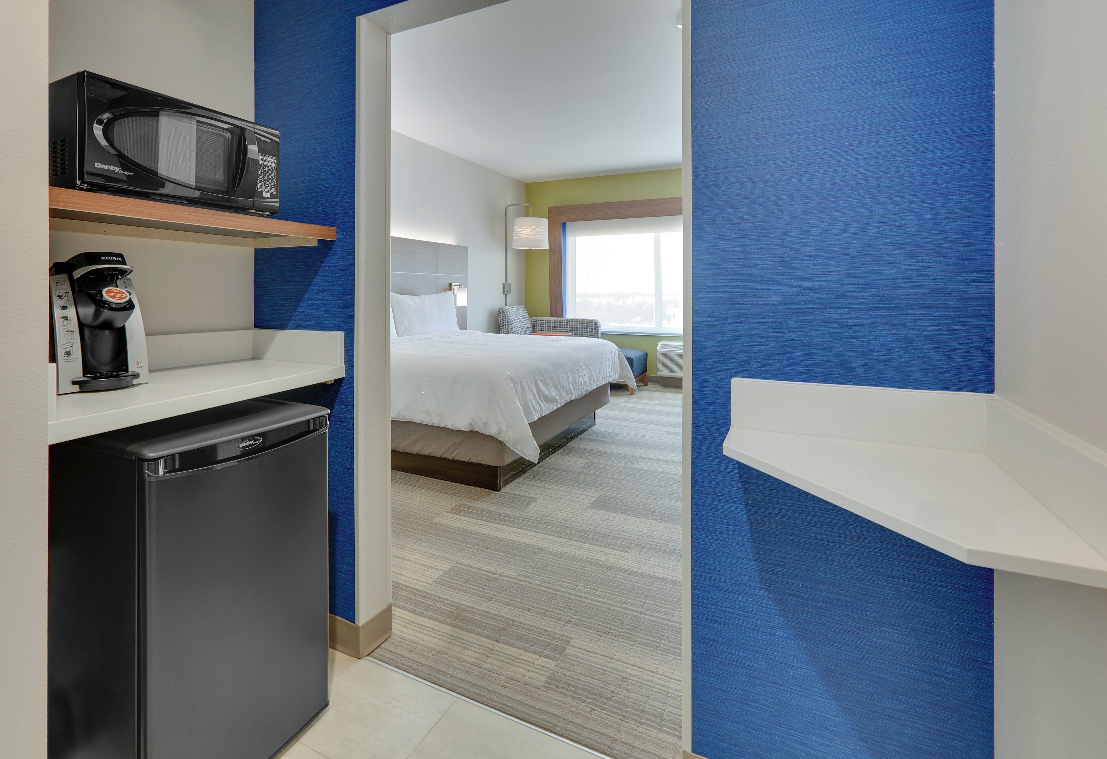 A hotel room with a bed, a microwave, a coffee machine, and a small kitchenette area.
