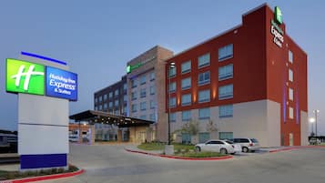 A Holiday Inn Express & Suites hotel with a modern design, featuring a prominent entrance and a parking area.