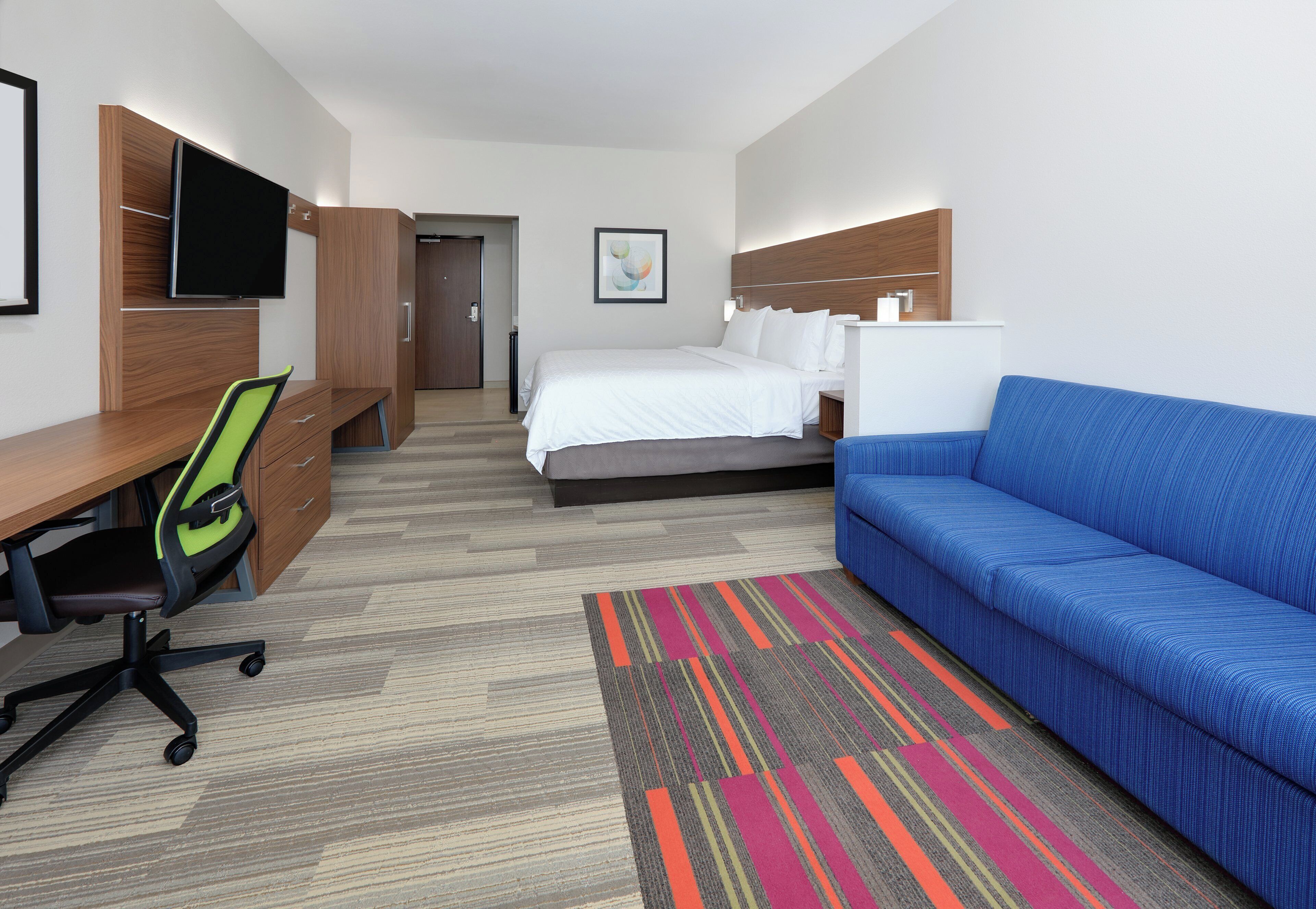 Una habitación de hotel con cama, escritorio y silla, sofá azul, televisión y puerta.