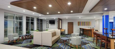 Een moderne hotel lobby met een grote bank, ronde tafels en een kamerbreed tapijt met dessin.
