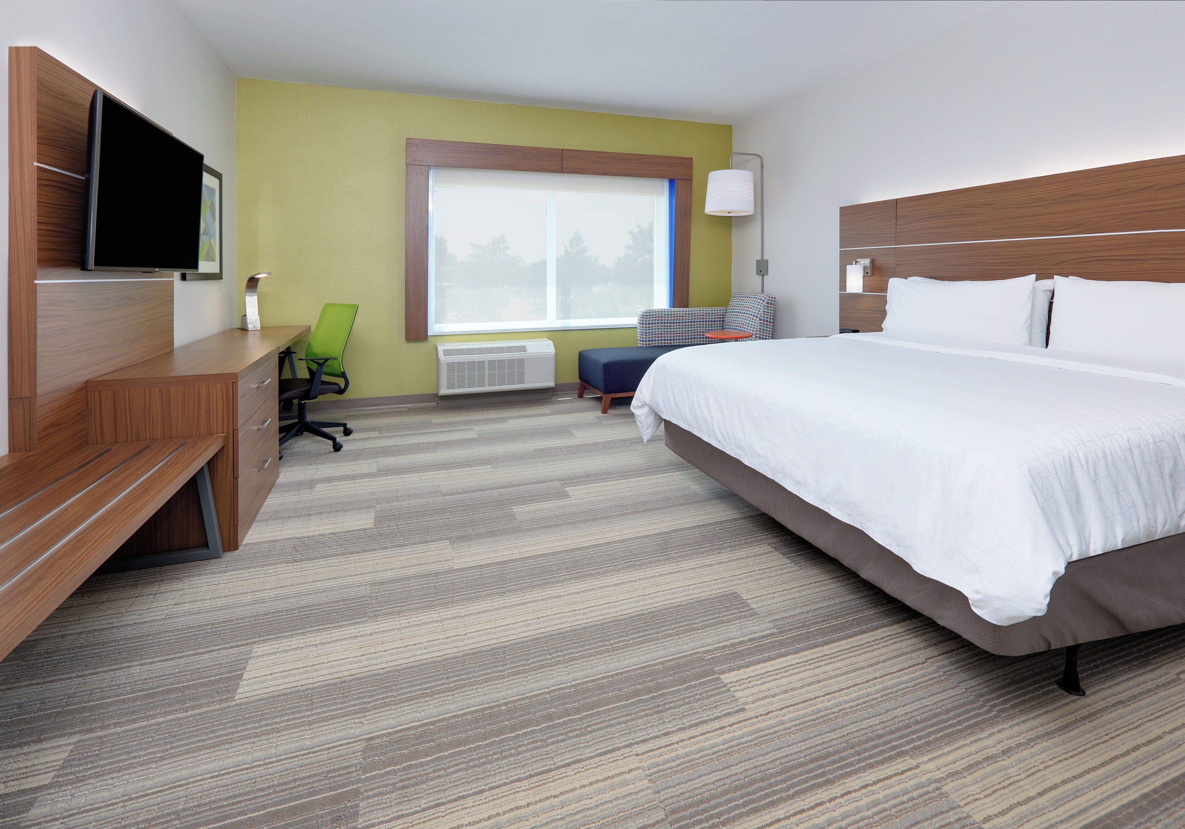 A hotel room with a bed, desk, chair, and a large window.
