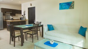 A modern living room with a white sofa, blue cushions, a glass coffee table, and a dining area with a glass table and chairs. - Apartamento PlayaDelCarmen 489 by Sinbad (Playa del Carmen)