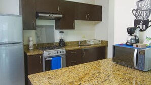 A compact kitchen with a refrigerator, stove, microwave, and a coffee maker on the counter. - Apartamento PlayaDelCarmen 489 by Sinbad (Playa del Carmen)