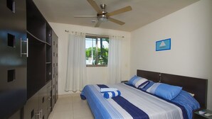 A hotel room with a bed, a ceiling fan, a window with curtains, a nightstand, and a wardrobe. - Apartamento PlayaDelCarmen 489 by Sinbad (Playa del Carmen)