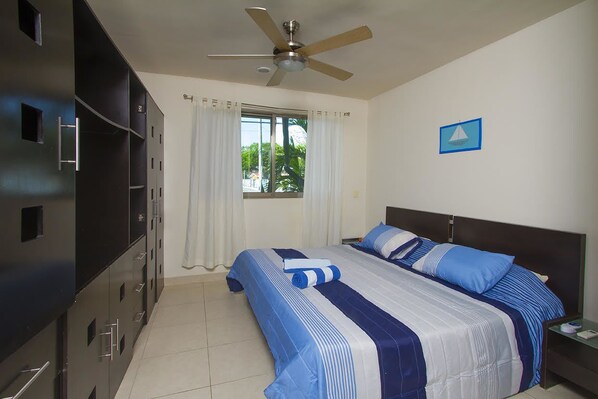 A hotel room with a bed, a ceiling fan, a window with curtains, a nightstand, and a wardrobe.