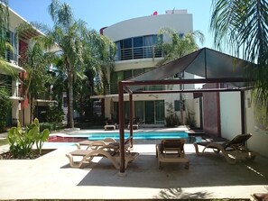 A pool area with lounge chairs and a shaded structure.