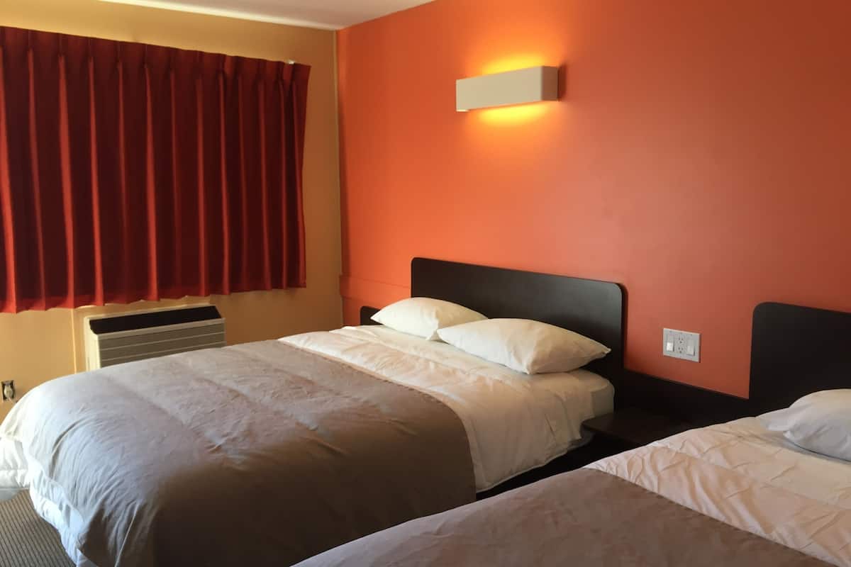 Habitación de hotel con dos camas, una cortina roja, una lámpara fijada a la pared y un enchufe.