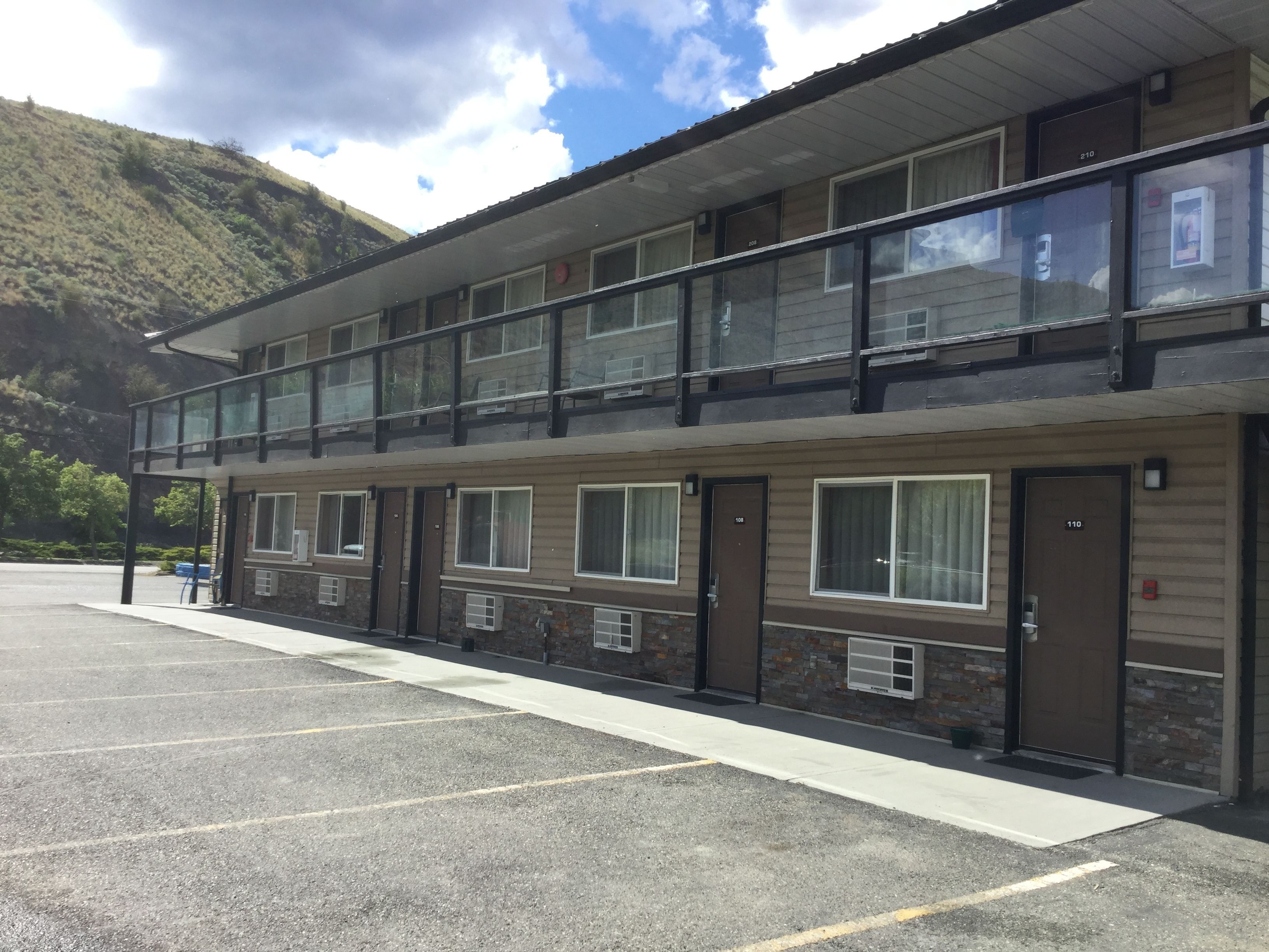 Ein Motel mit zweistöckiger Struktur, mehreren Zimmern und einem Parkplatz.