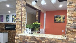 A reception area with a stone wall, a counter with informational brochures, a potted plant, and a television mounted on the wall. - Riverside Motel (Cache Creek)