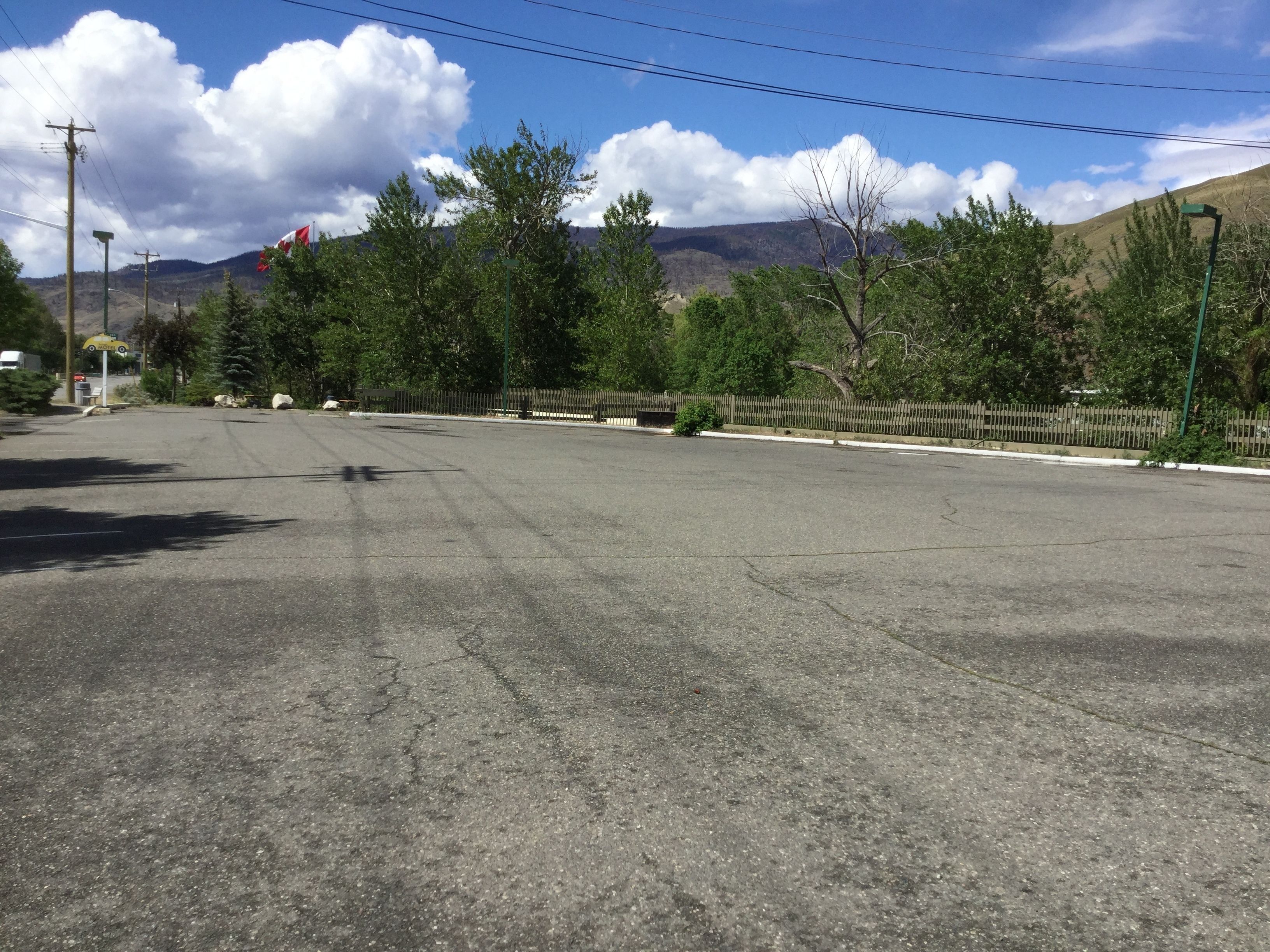 A wide, empty road with a Canadian flag, trees, and a mountain in the background.