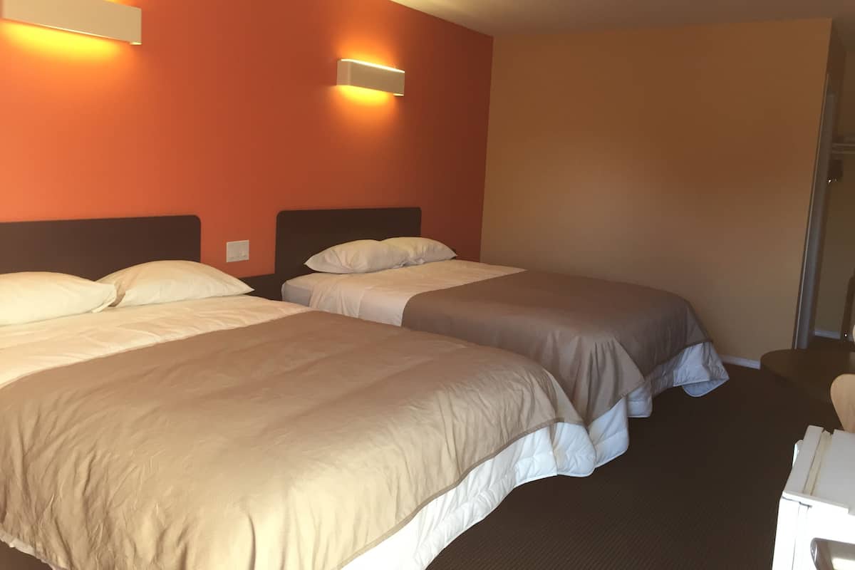 Habitación de hotel con dos camas, cada una con cabecera y almohadas, y dos lámparas fijadas a la pared.