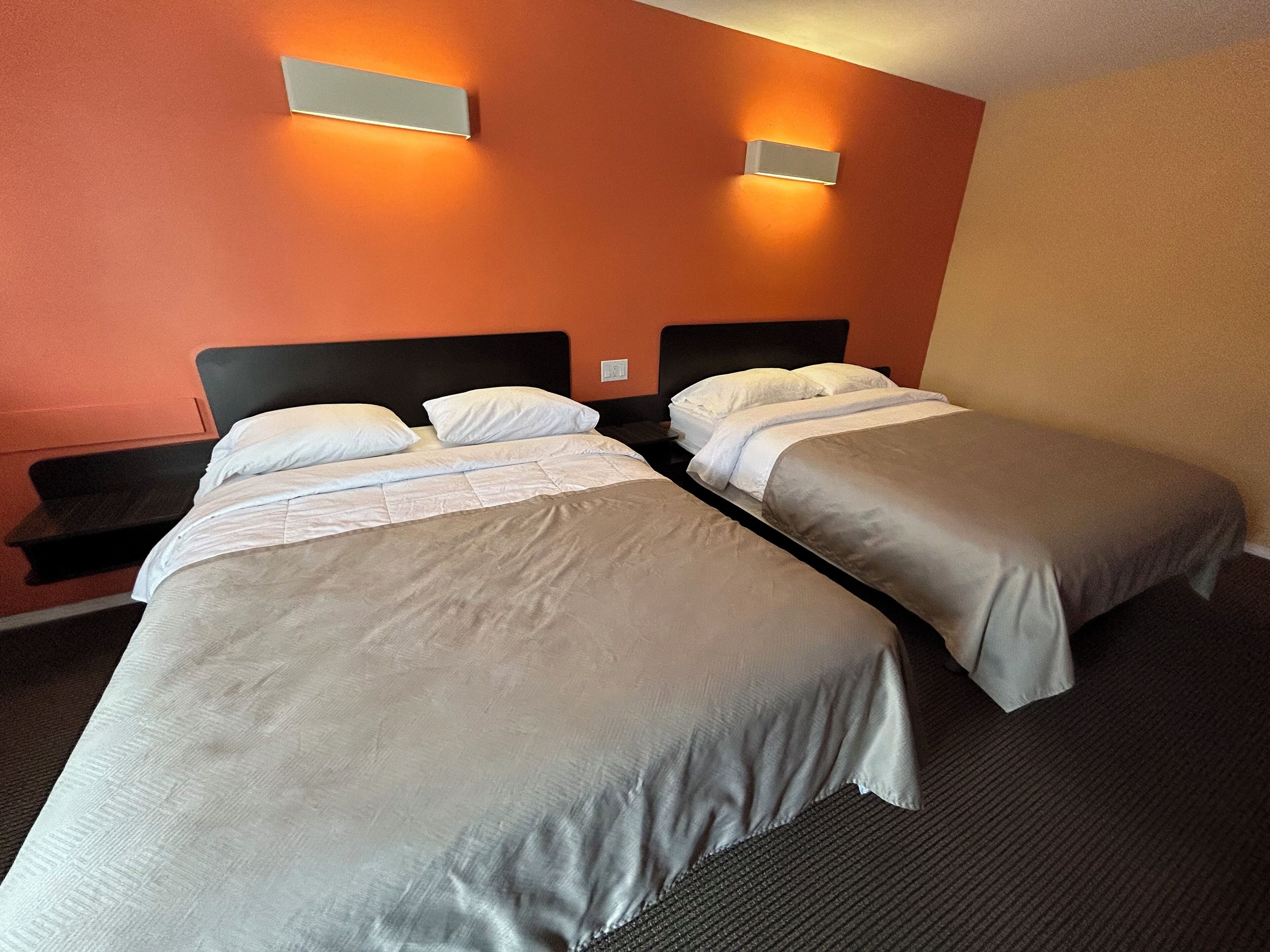A hotel room with two beds, a nightstand, and two wall-mounted lights.