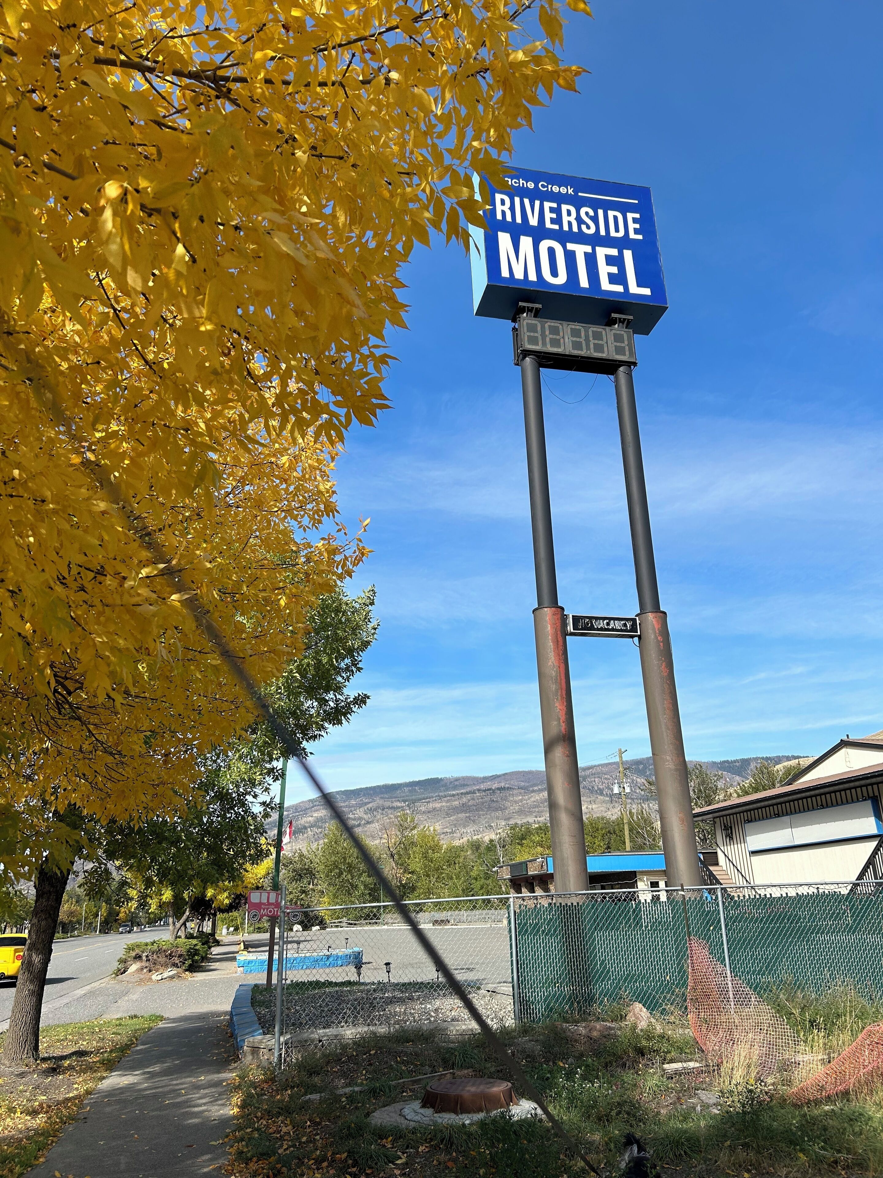 A sign for Riverside Motel with a clear view of the surrounding area including a road, a fence, and a distant landscape.